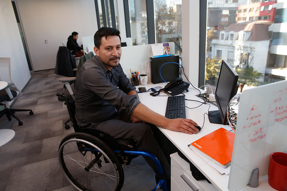 persona con discapacidad en silla de ruedas trabajando en una oficina frente a un computador