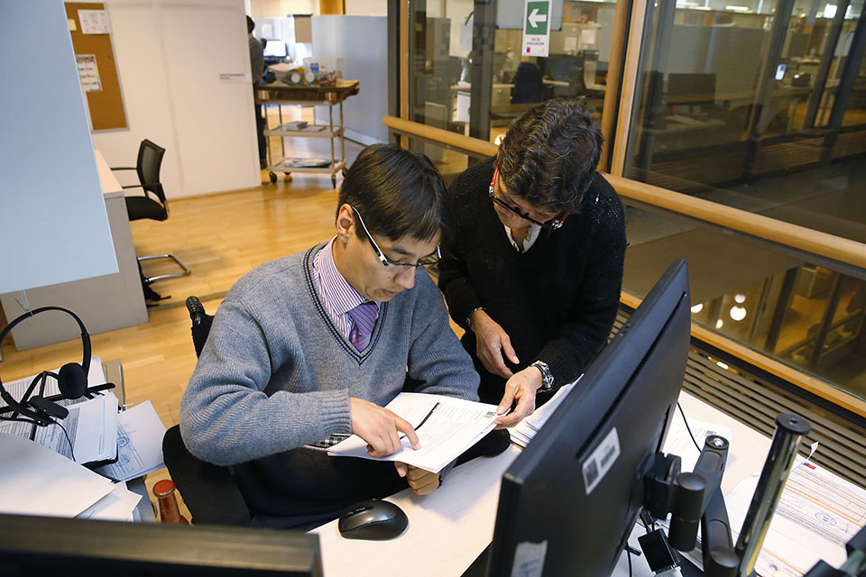 persona con discapacidad en silla de ruedas junto a otra persona revisan un documento en una oficina frente a un computador