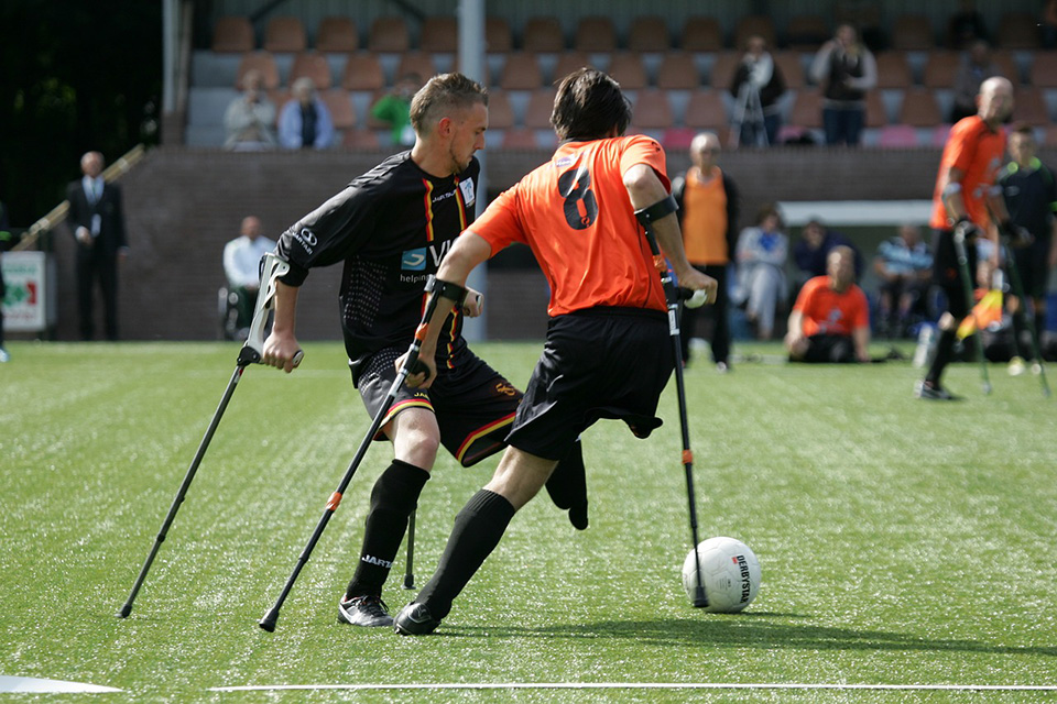 Dos personas con una pierna y bastones jugando fútbol